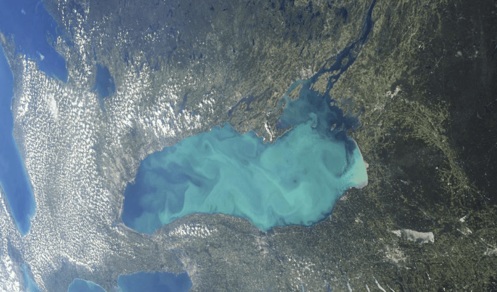 Vue aérienne du lac avec des eaux turquoise entourées de terre verdoyante et de nuages.